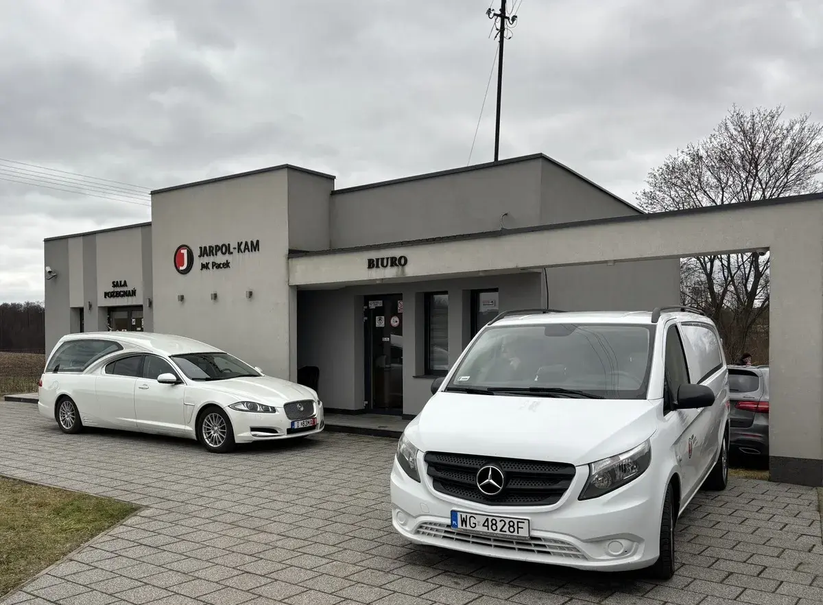 Przed budynkiem "JARPOL-KAM" stoją karawan i van. Firma zajmuje się transportem zmarłych, odpowiadając na pytanie, kto pokrywa koszty sprowadzenia zwłok z zagranicy.