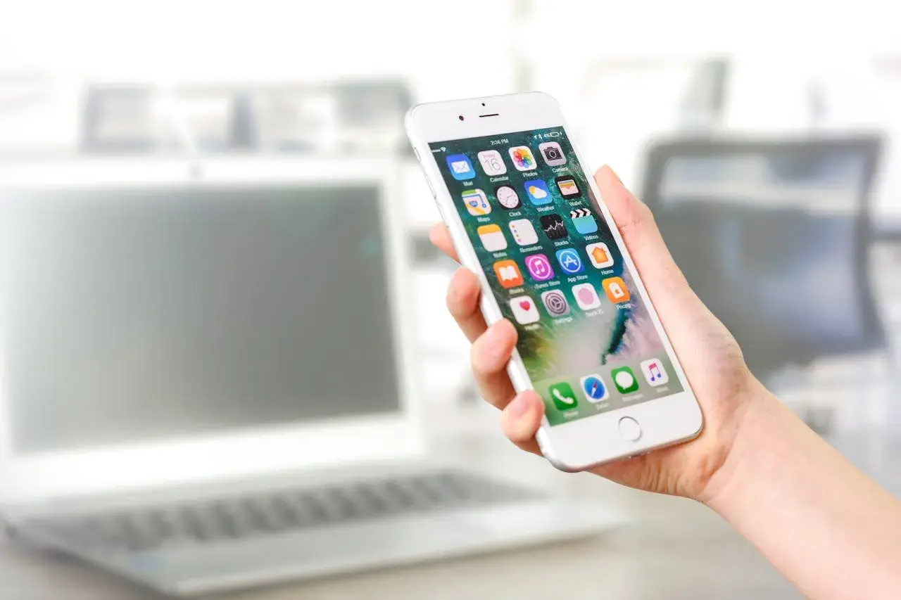 Dłoń trzyma iPhone'a z ikonami aplikacji. Dowiedz się, jak włączyć lokalizację w przeglądarce iPhone, aby korzystać z map i innych funkcji.