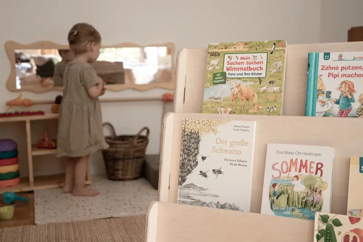 Ein kleines Mädchen in einer Montessori Kita entdeckt Bücher über Tiere und den Sommer.