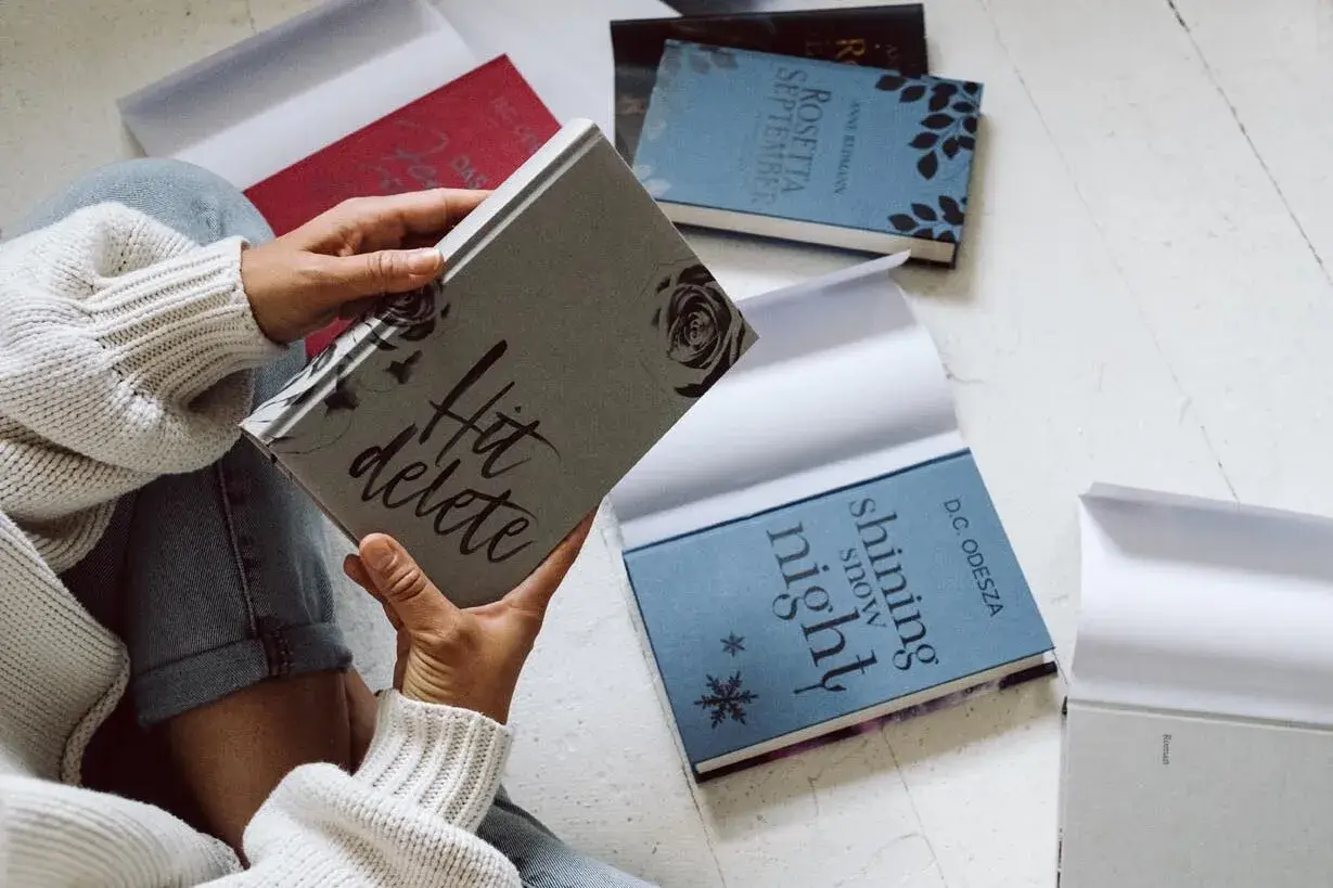 Une personne feuillette des livres aux couvertures élégantes, dont "Hit delete" et "Shining snow night". Ces éditions font partie des plus belles éditions de livres.