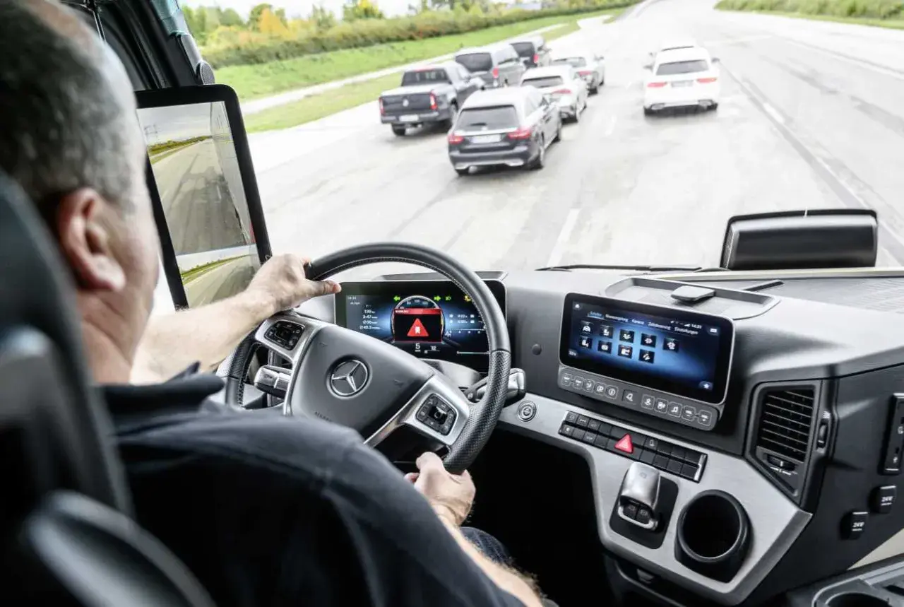 Fahrer im LKW-Cockpit mit Blick auf die Straße und ein Display, das die allgemeine Sicherheitsvorschrift anzeigt.