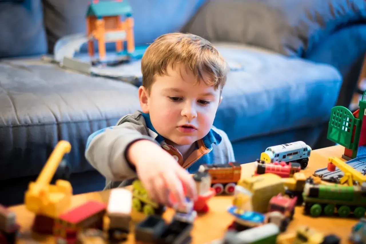 Bambino concentrato nel suo gioco del far finta con tanti trenini e costruzioni colorate.