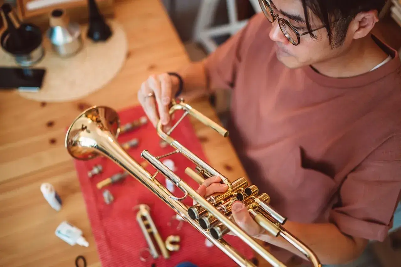 Un homme nettoie son instrument cuivre, une trompette, sur une table en bois.