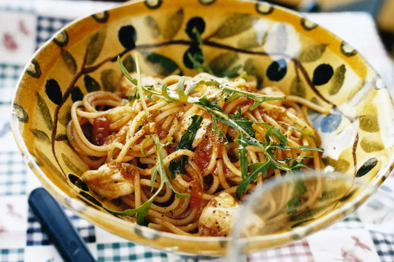En skål med spaghetti med tomatsås, toppad med ruccola och strödd med svartpeppar. En härlig pasta med tomatsås som ser utsökt ut.