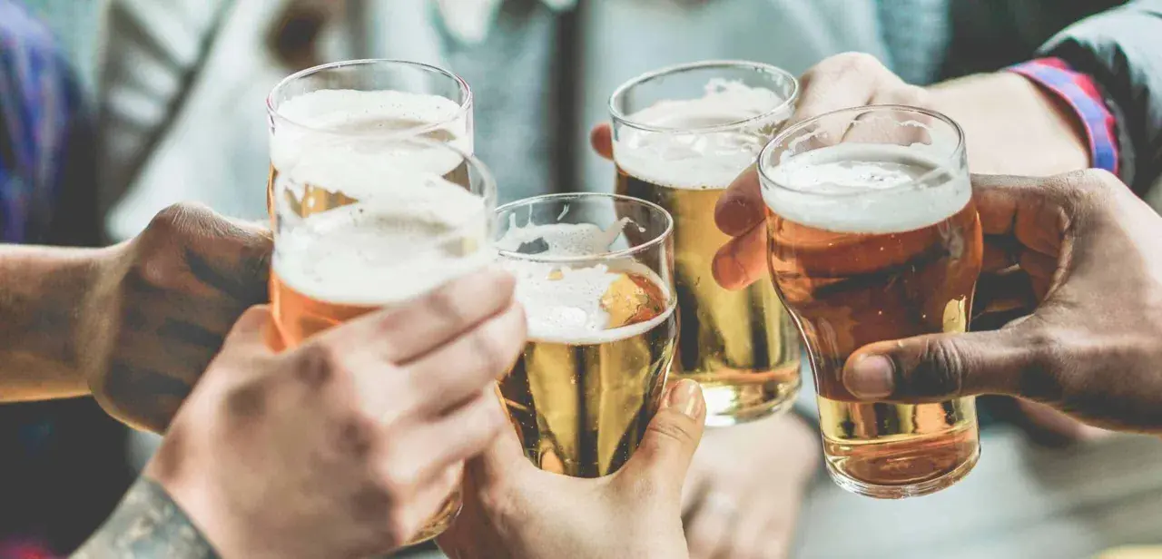Brindisi con birra, un piacere che, si dice, la birra fa ingrassare. Mani che sollevano bicchieri dorati con schiuma bianca.