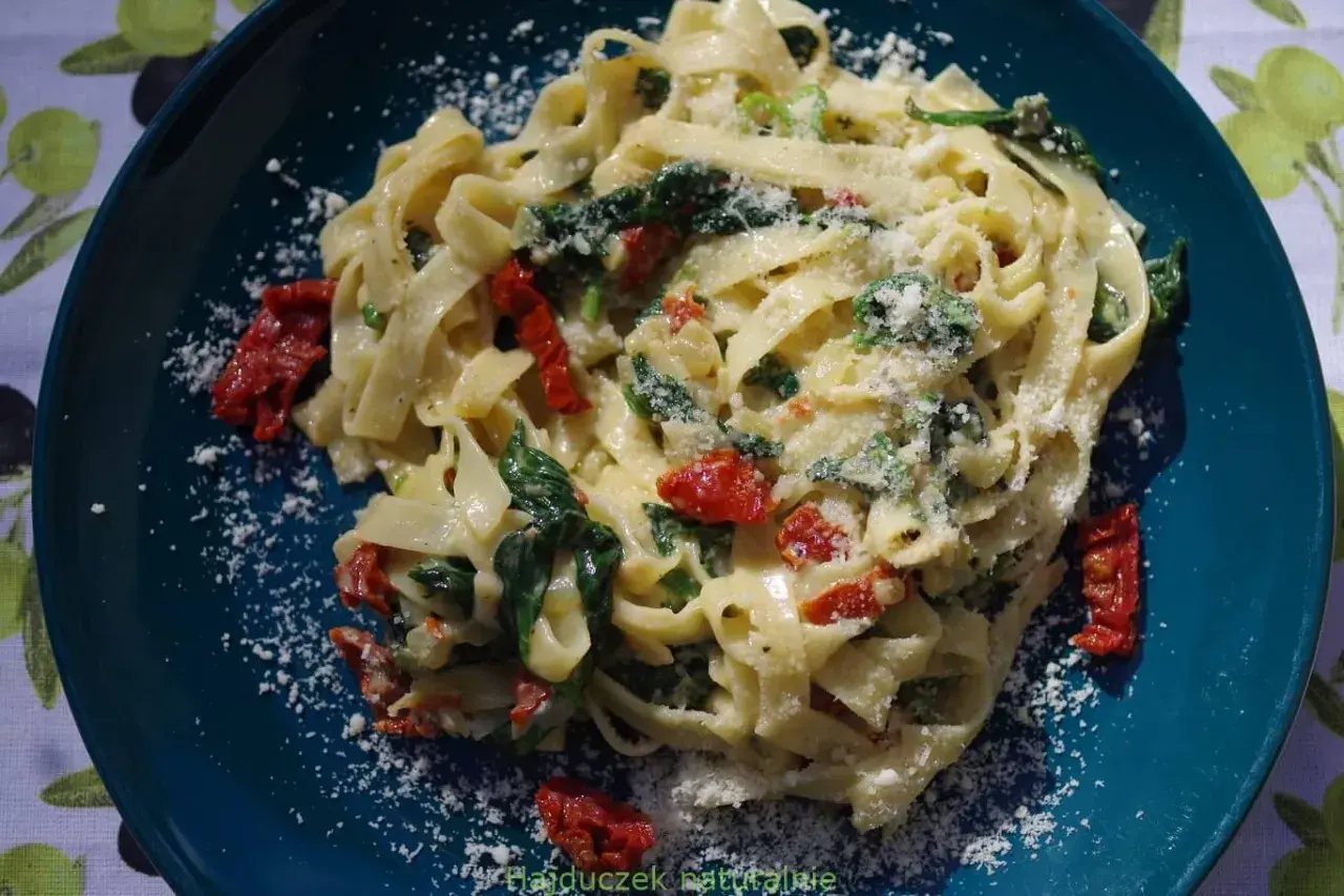 Pyszny makaron tagliatelle ze szpinakiem i suszonymi pomidorami, posypany parmezanem. Idealny na szybki obiad.