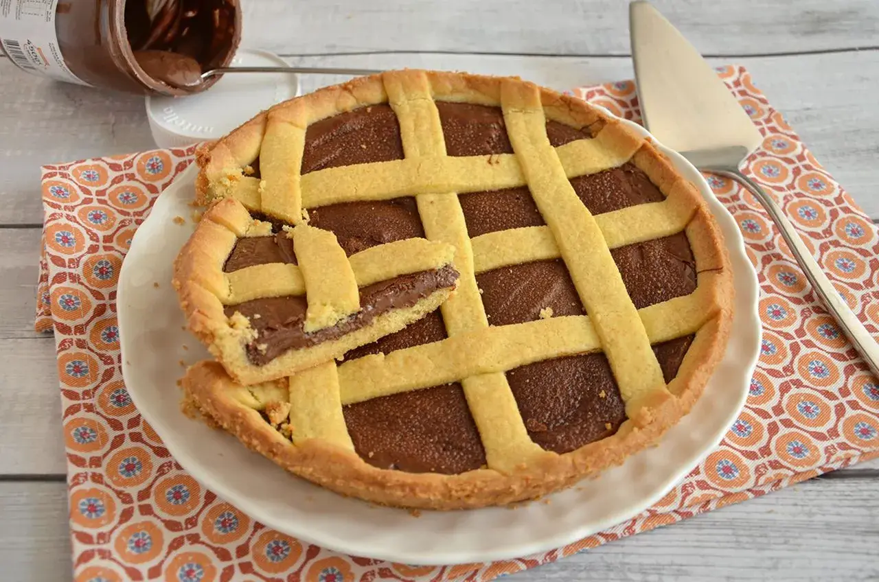 Deliziosa crostata alla Nutella con una fetta tagliata, pronta per essere gustata. Un vasetto di Nutella è visibile sullo sfondo.