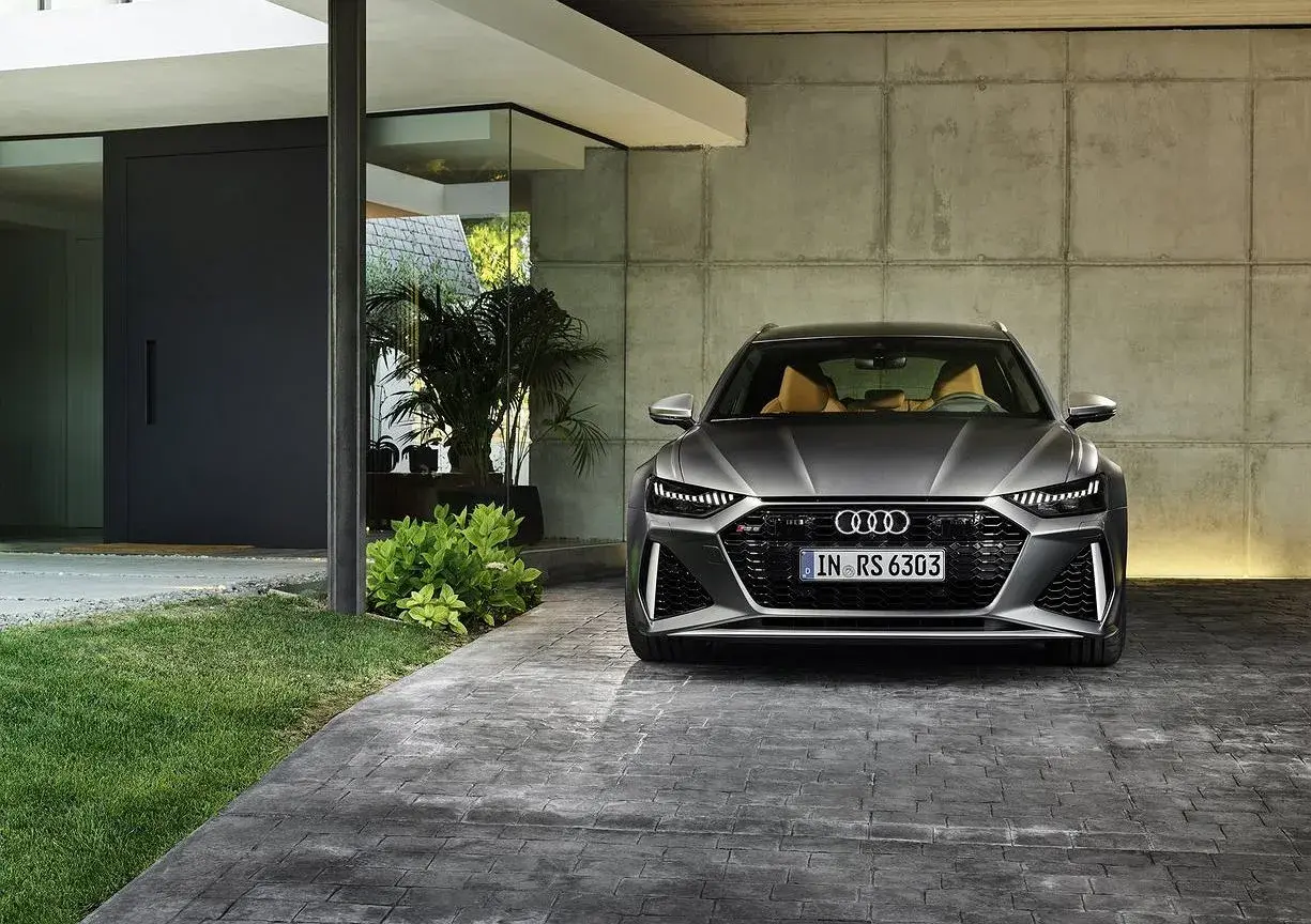 Szary Audi RS6 Avant z beżowym wnętrzem zaparkowany przed nowoczesnym domem. Sprawdź audi rs6 cena.