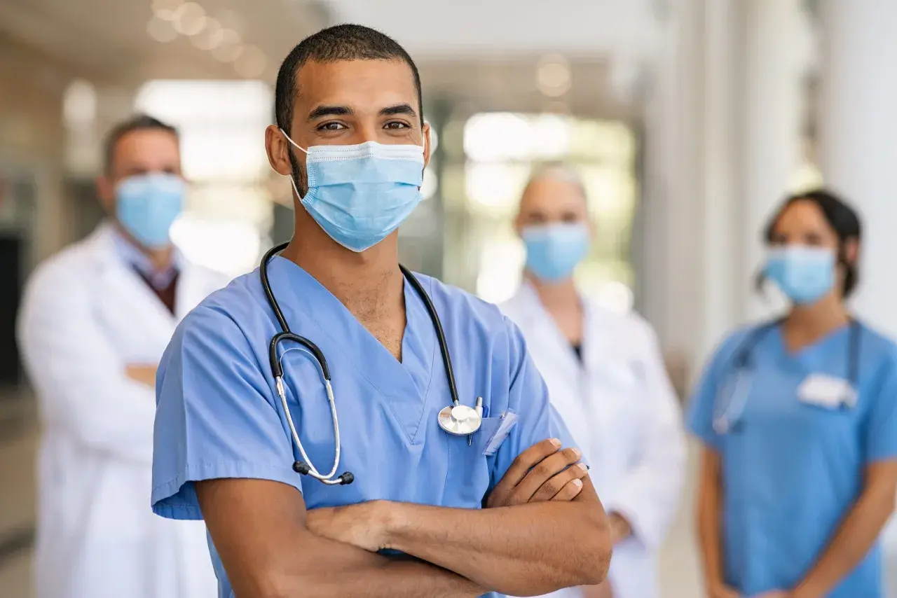 Un medico dello sport sorride, con colleghi sullo sfondo. Lo stipendio di un medico dello sport è una ricompensa per la dedizione.