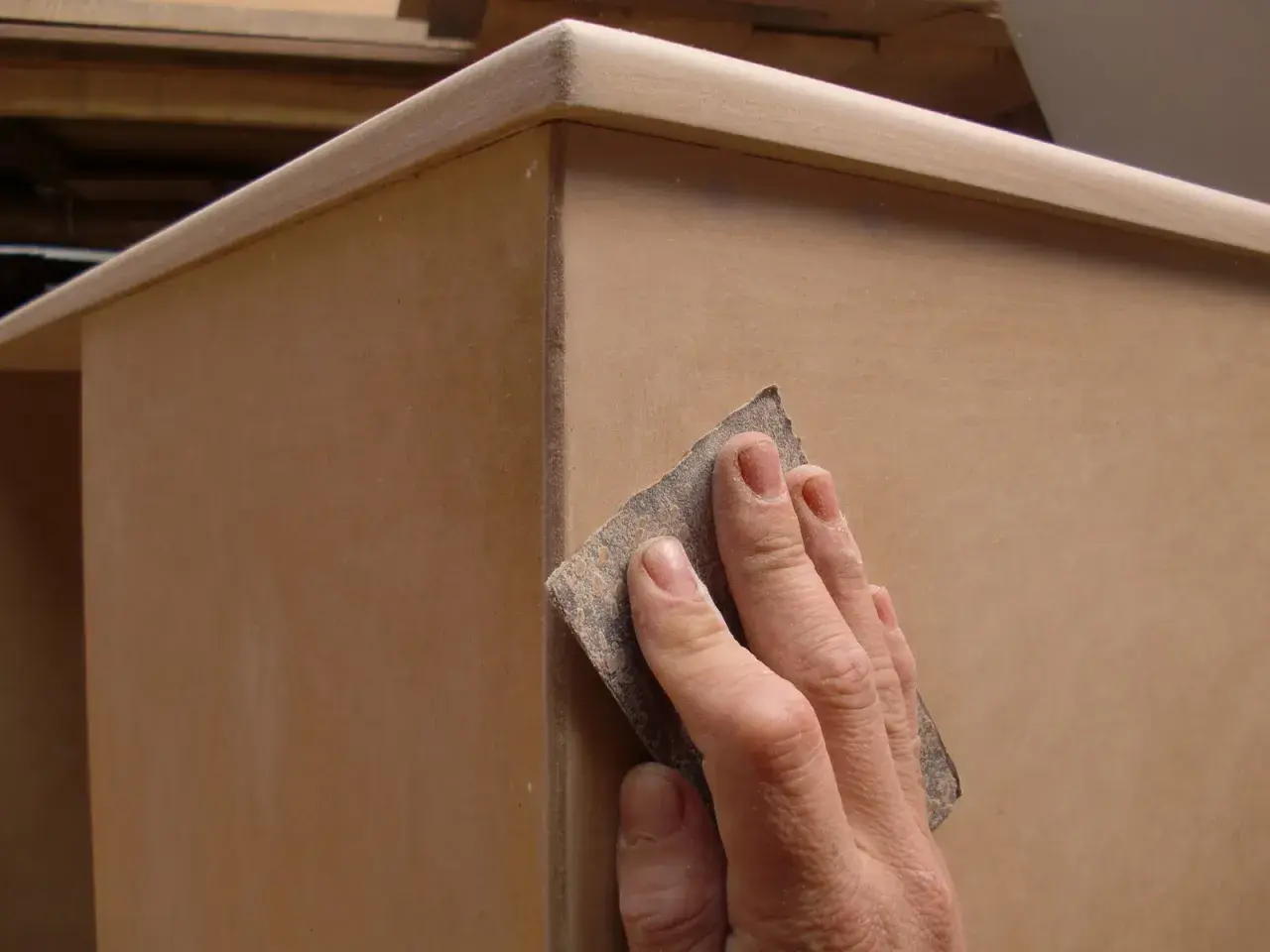 Mano lijando un mueble de mdf para prepararlo antes de pintar.