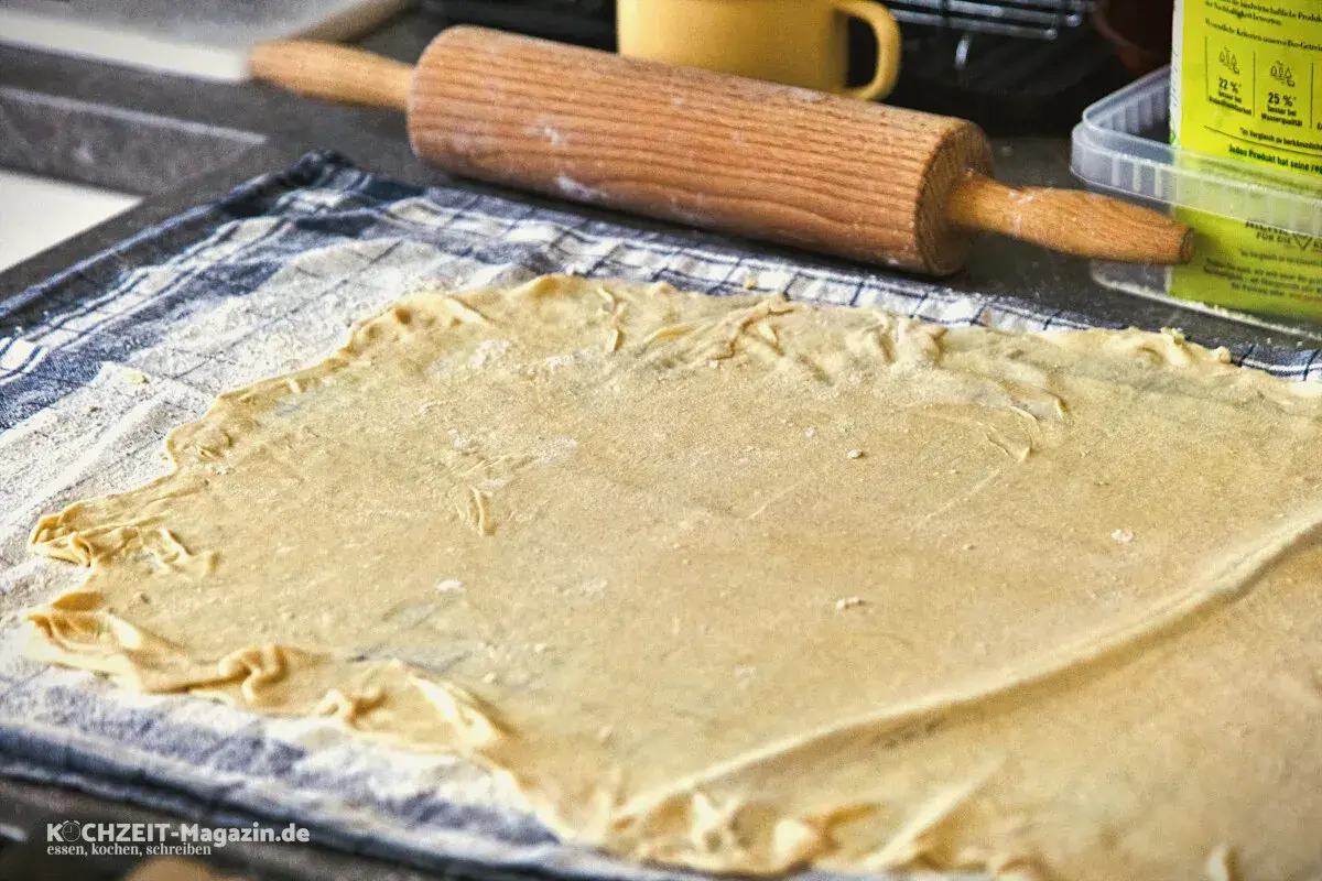 Dünn ausgerollter Strudelteig liegt auf einem Küchentuch, bereit für ein köstliches Strudel-Rezept. Ein Nudelholz liegt daneben.