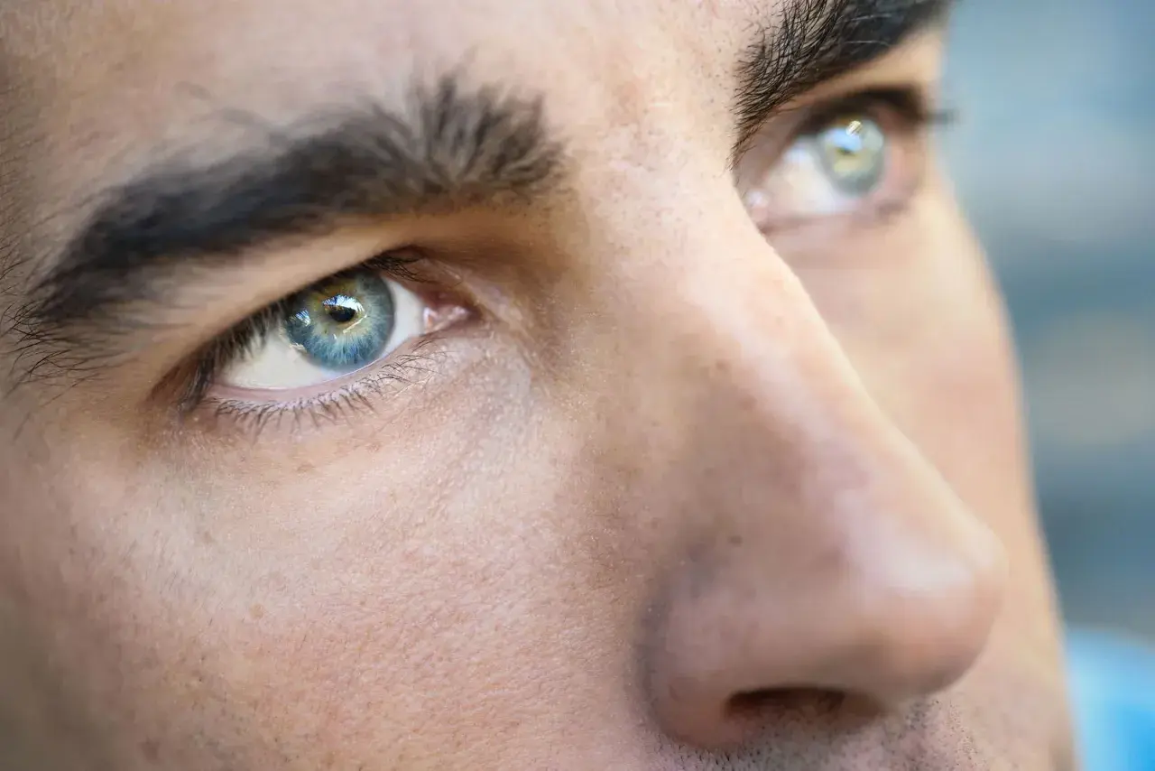 Primer plano de los ojos de un hombre, destacando sus cejas pobladas y el iris azul verdoso.