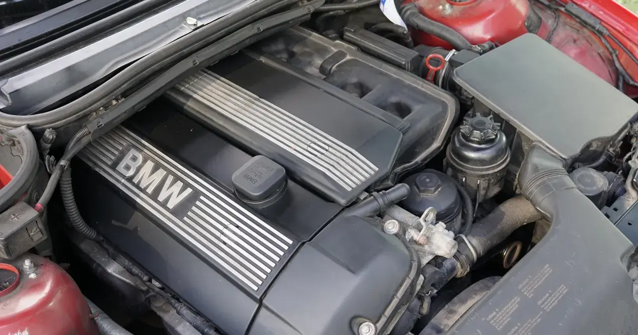 Silnik BMW e46, widok z góry. Czarna pokrywa silnika z napisem BMW i metalowymi wstawkami. Widać też elementy układu dolotowego i zbiorniczek płynu.