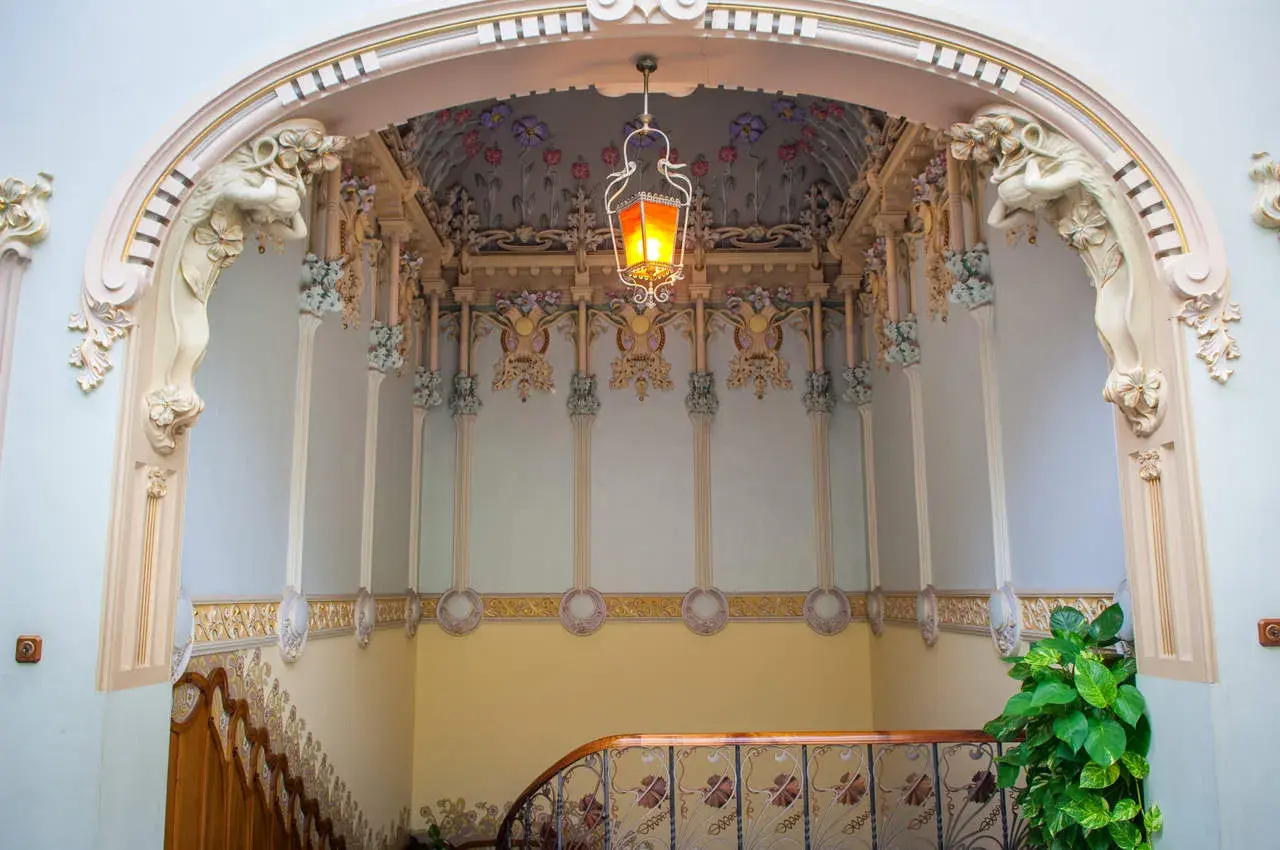 Detalles ornamentales de una casa modernista en Novelda, con una lámpara colgante y motivos florales en el techo.
