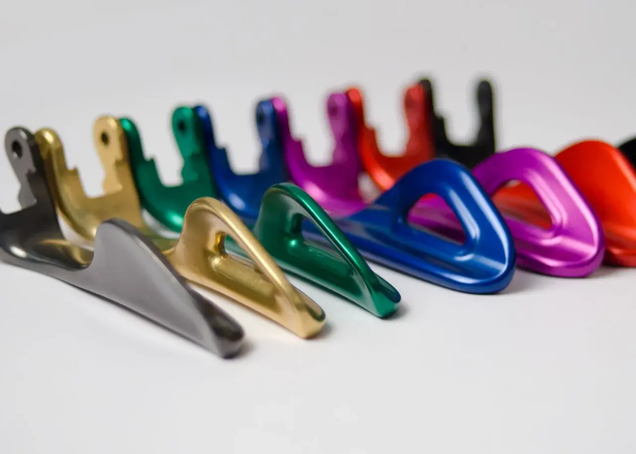 Una fila di moschettoni colorati, con finitura anodizzazione naturale, disposti su sfondo bianco.