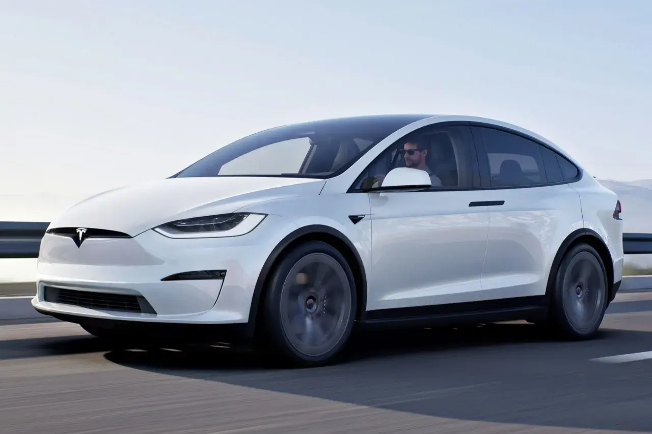 Biały Tesla X w ruchu. Kierowca w okularach przeciwsłonecznych. Sprawdź aktualną tesla x cena i możliwości tego SUV-a.