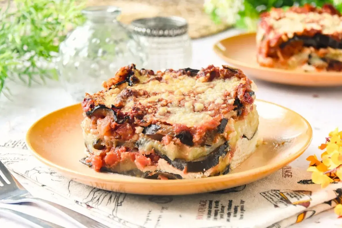 Porción de lasaña de berenjena horneada, con capas de berenjena, salsa de tomate y queso derretido, servida en un plato naranja.
