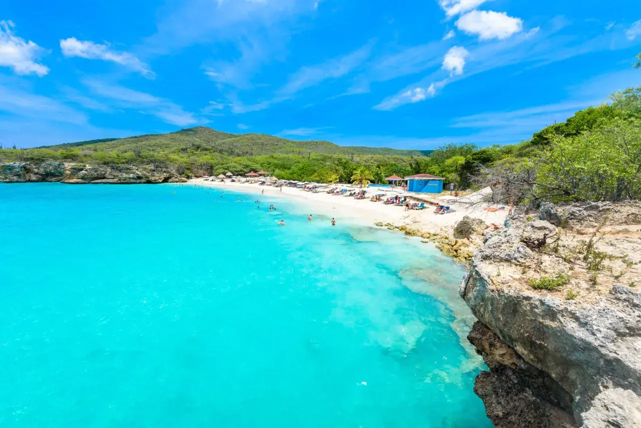 Traumhafter Curacao Beach mit türkisblauem Wasser, weißem Sand, Liegestühlen und Menschen, die schwimmen und sich sonnen.