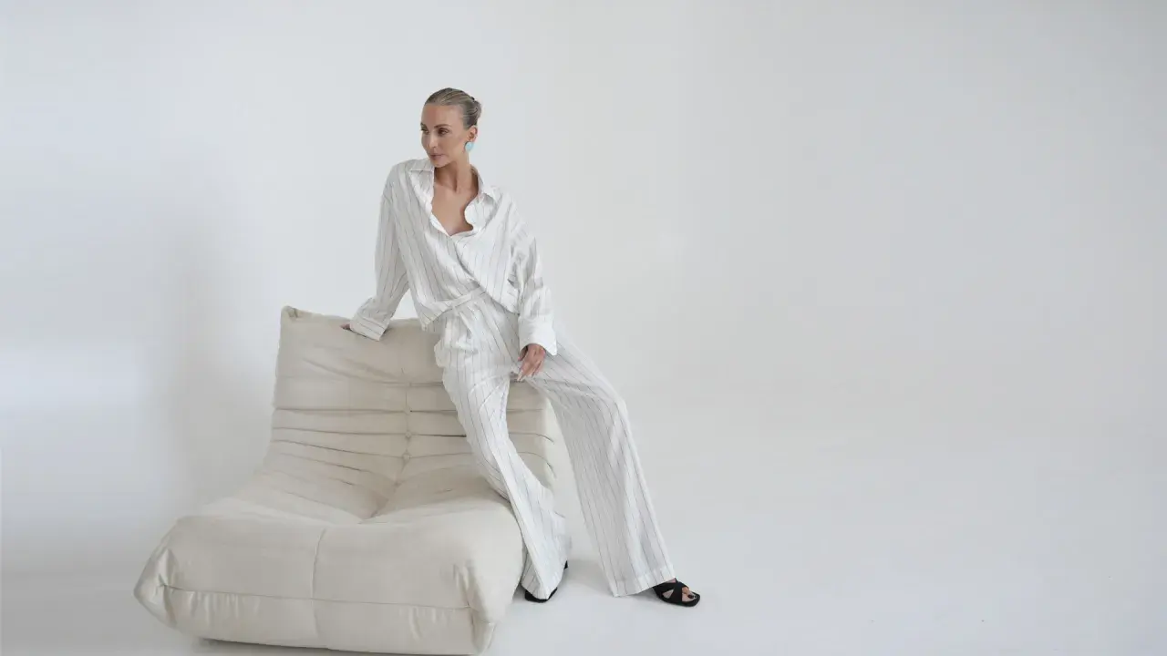 Elegancka kobieta w pasiastym komplecie, uosobienie quiet luxury, siedzi na kremowej sofie.
