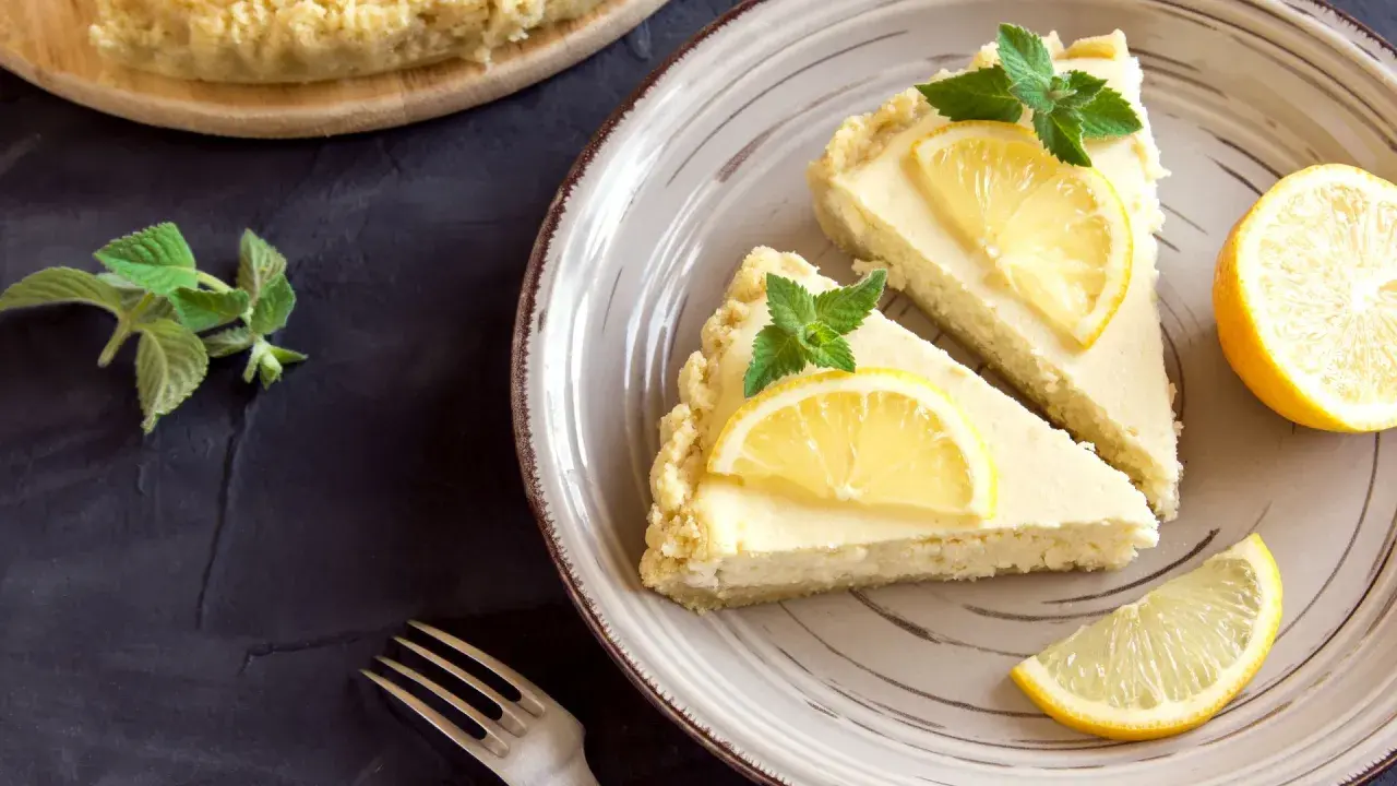 Dos porciones de tarta de limón, decoradas con rodajas de limón y hojas de menta, listas para ser disfrutadas.