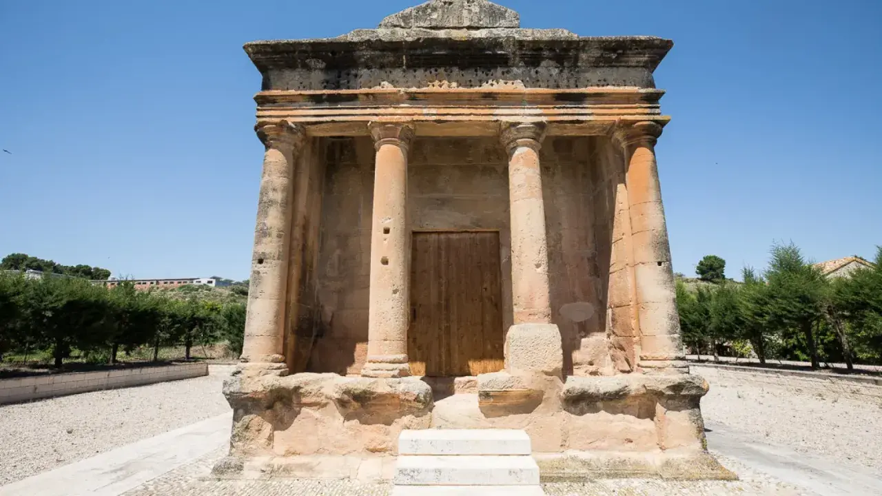 El mausoleo de Fabara, con sus columnas y puerta de madera, se alza imponente bajo un cielo azul.