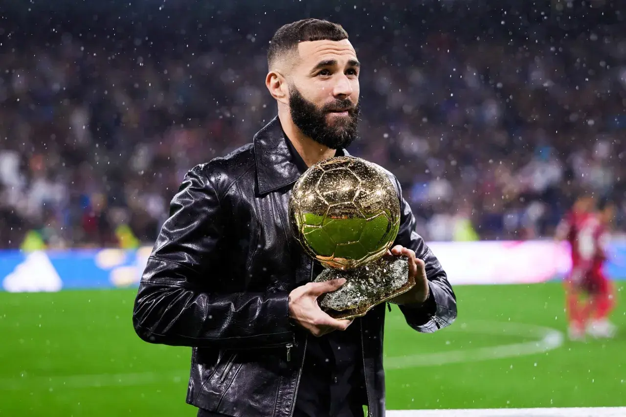 Karim Benzema trzyma Złotą Piłkę, zastanawiając się, ile waży złota piłka.