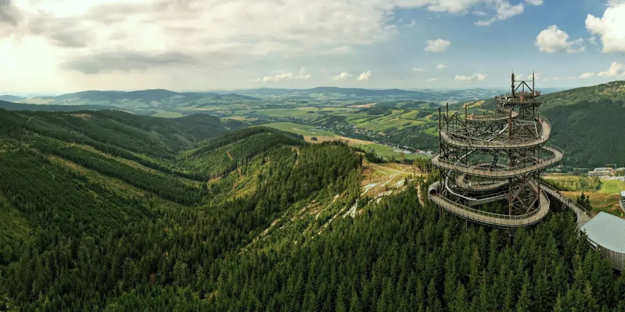 Widok na Sky Walk w Czechach, spiralną wieżę widokową pośród zielonych lasów i pagórków.