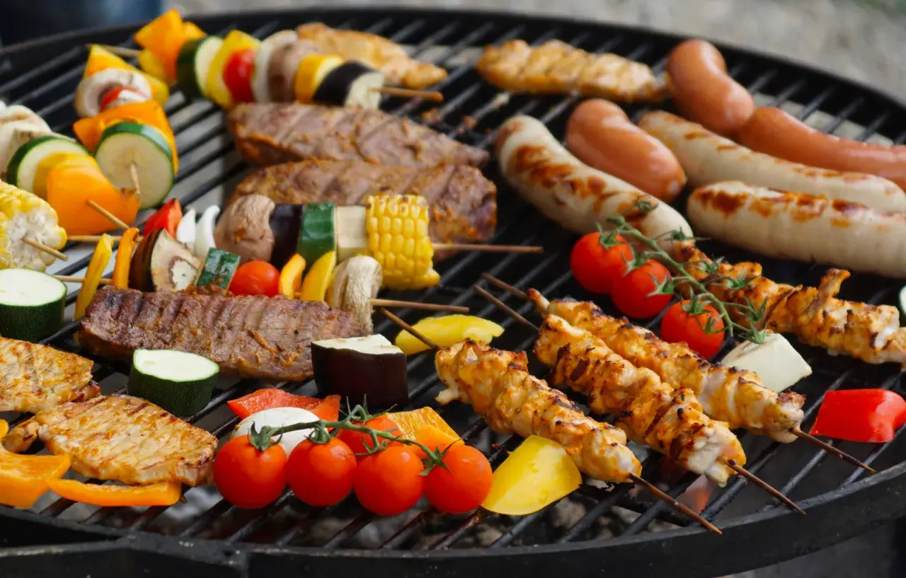 Un festin de Noël en plein air : brochettes de poulet, saucisses, steaks et légumes colorés sur un barbecue.