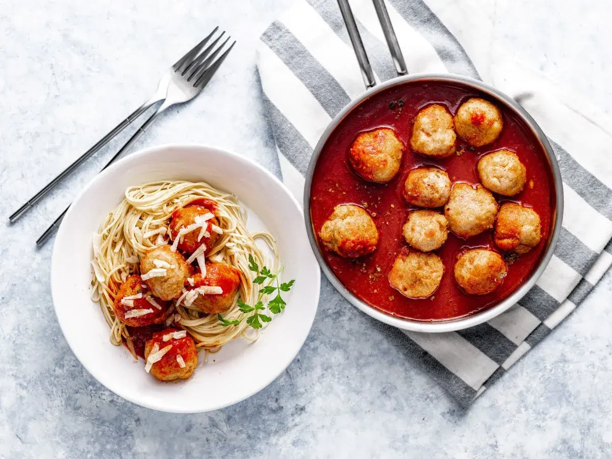 Pulpety w sosie pomidorowym na talerzu ze spaghetti i w rondelku.