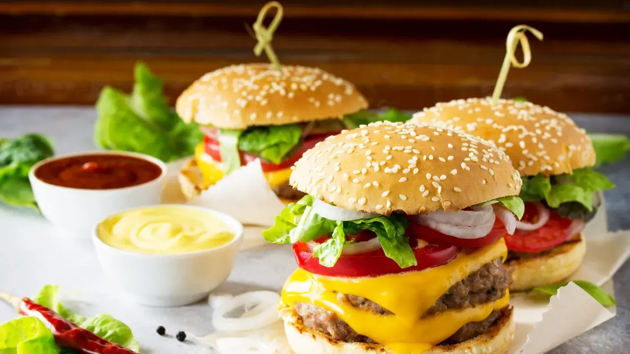 Tre succulenti burger roll con formaggio fuso, pomodoro, cipolla e lattuga, accompagnati da salse.
