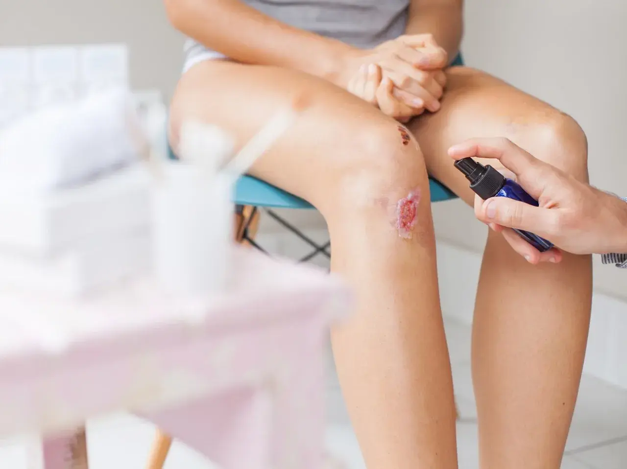 Jemand desinfiziert eine aufgeschürfte Wunde am Knie mit einem Spray.