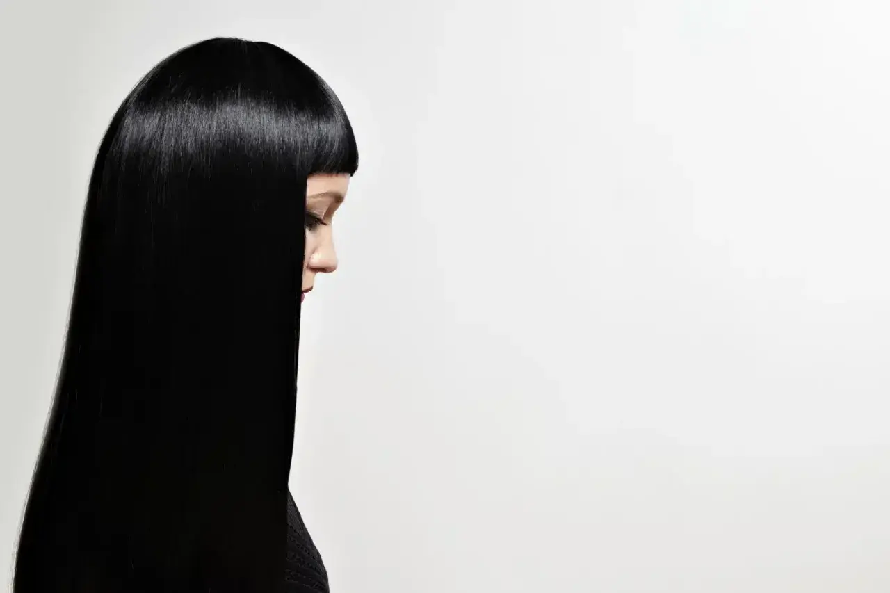 Perfil de mujer con cabello liso y brillante, negro azabache, cayendo sobre su hombro.