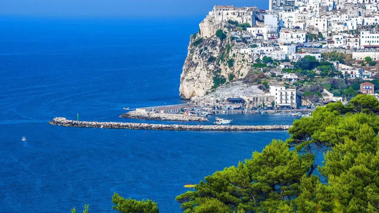 Rodi Garganico, Puglia: case bianche aggrappate alla scogliera, un porto con barche e il mare blu intenso.