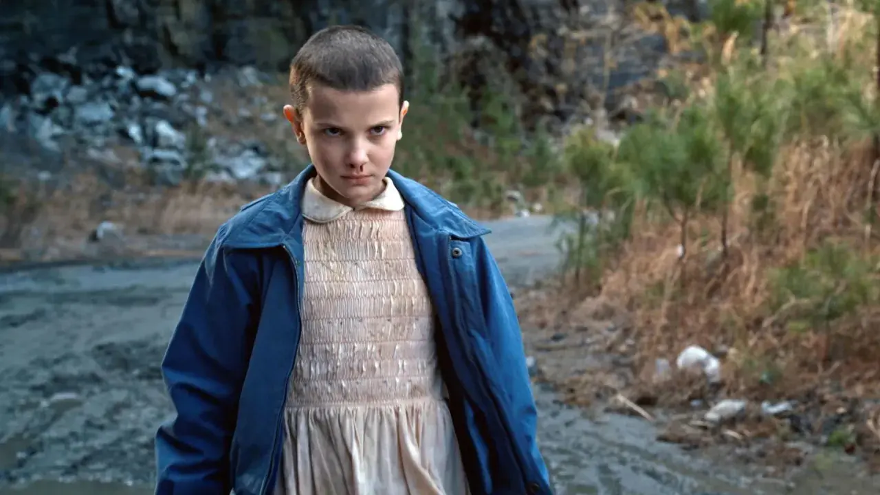 Nastka z Stranger Things, z nosem krwawiącym, stoi na brudnej drodze.