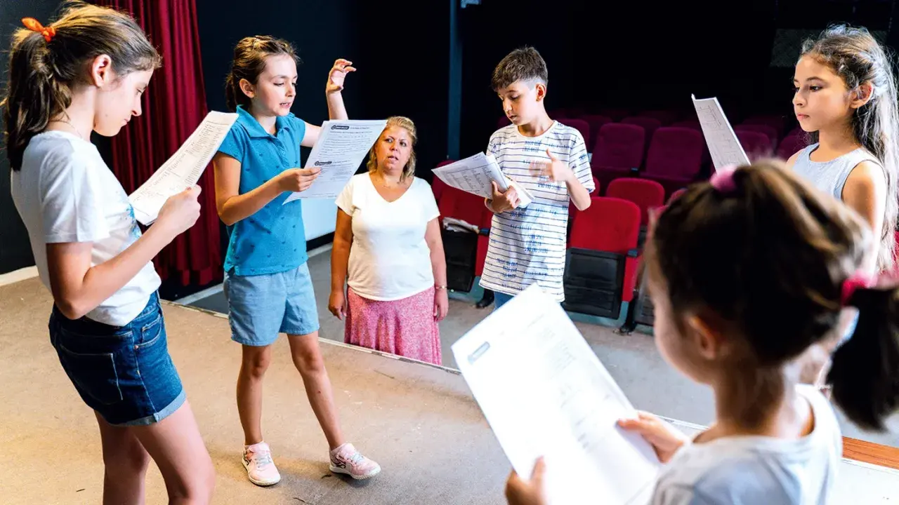 Kinder üben für ein **Vorlesetheater Grundschule**. Sie halten Texte in der Hand und schauen konzentriert.