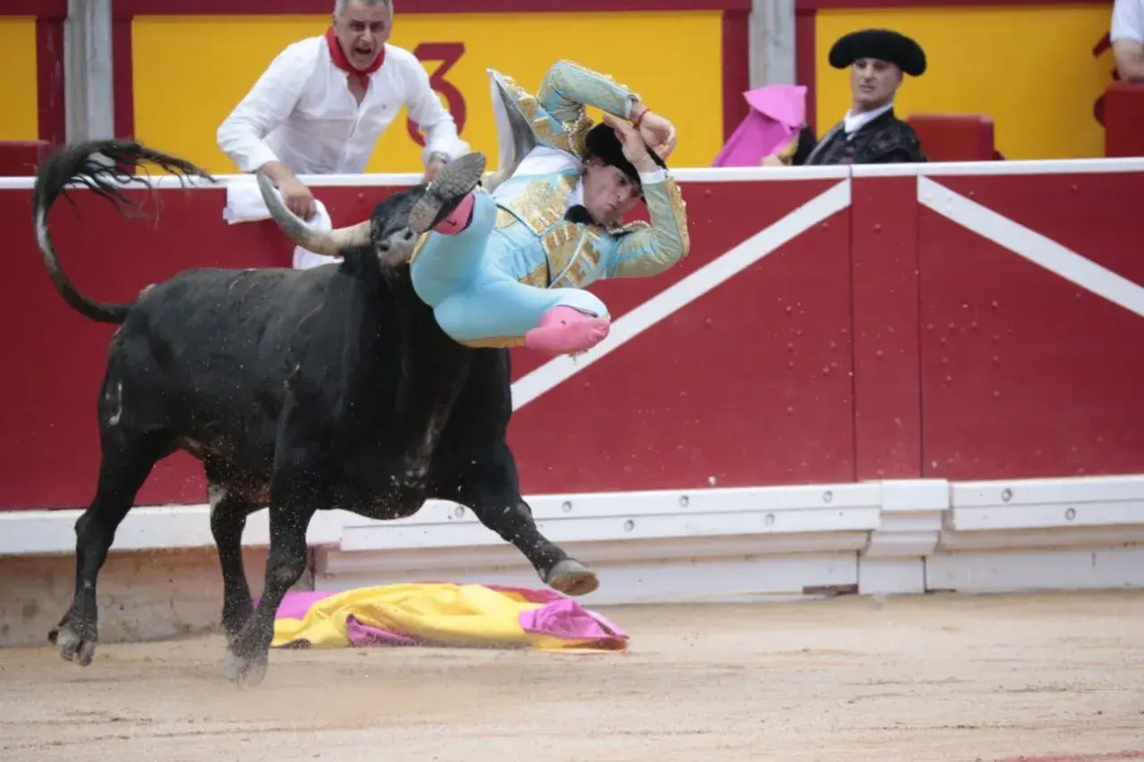 Un torero, Rubén Pinar, es lanzado por los aires por un toro negro en una plaza de toros.