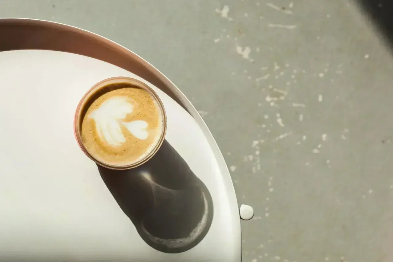 Idealny flat white z pianką w kształcie liścia, stojący na srebrnej tacy.