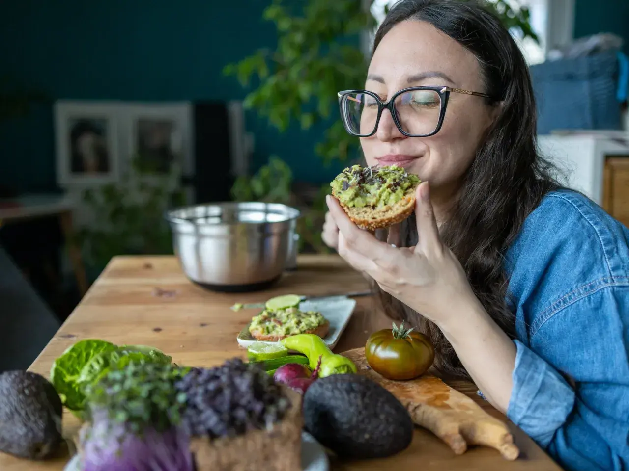 Frau genießt Avocado-Toast, ein gesunder Snack für das avocado abnehmen. Frische Zutaten liegen auf dem Tisch.