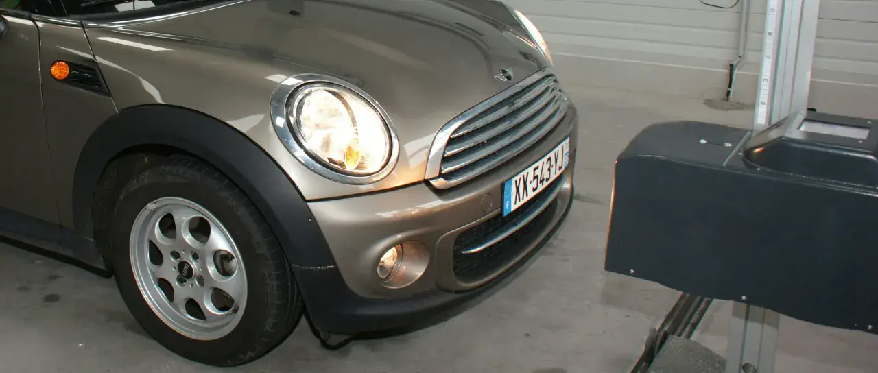 Réglage des feux diurnes d'une Mini Cooper marron, avec un appareil de mesure à droite.