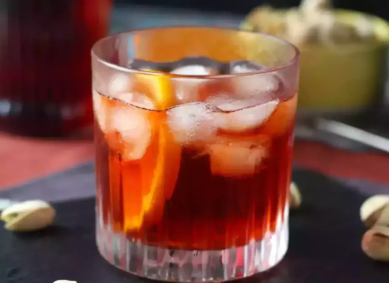 Klasyczny negroni przepis: czerwony koktajl z lodem i pomarańczą w szkle, obok pistacje.