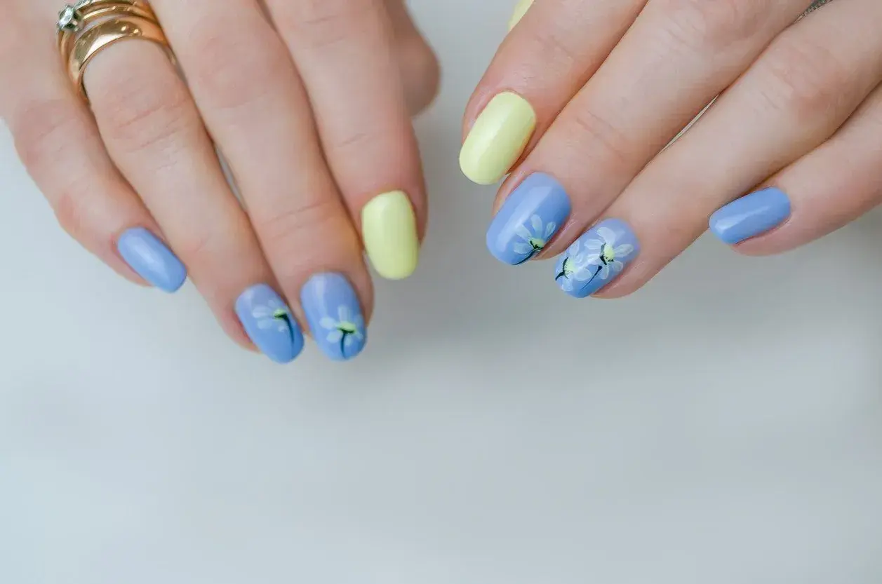 Delikatne kwiaty na paznokciach w pastelowych kolorach: błękitnym i żółtym. Wiosenny manicure z motywem stokrotek.