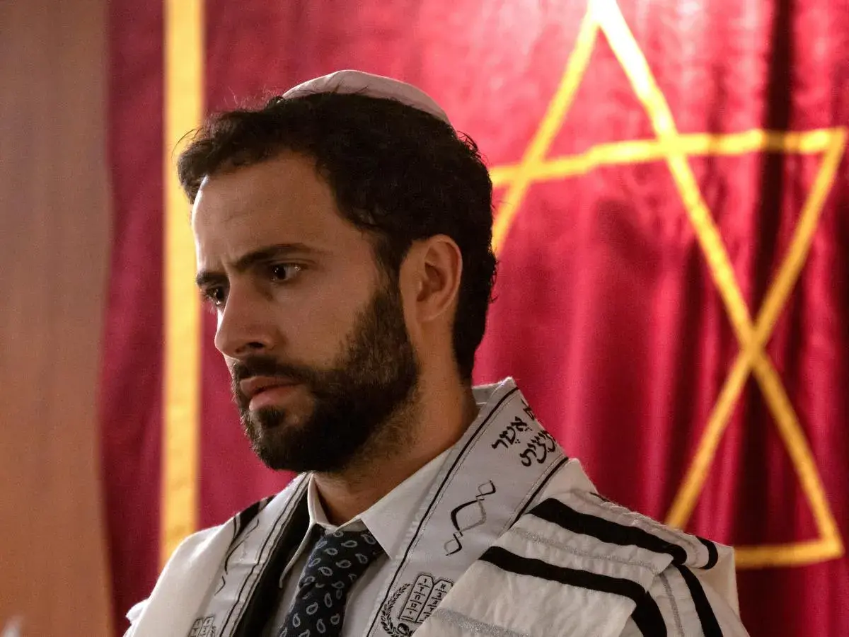 Ein Mann mit Bart und Kippa trägt einen Tallit. Im Hintergrund ist ein Davidstern auf rotem Stoff zu sehen. So sieht ein Jude aus.