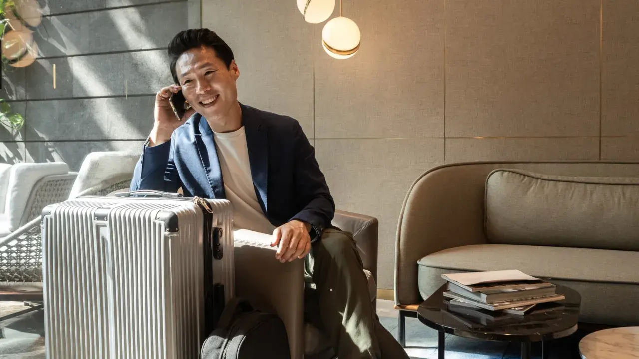 Mann telefoniert in der **Priority Pass Lounge** neben seinem silbernen Koffer. Entspannt wartet er auf seinen Flug.