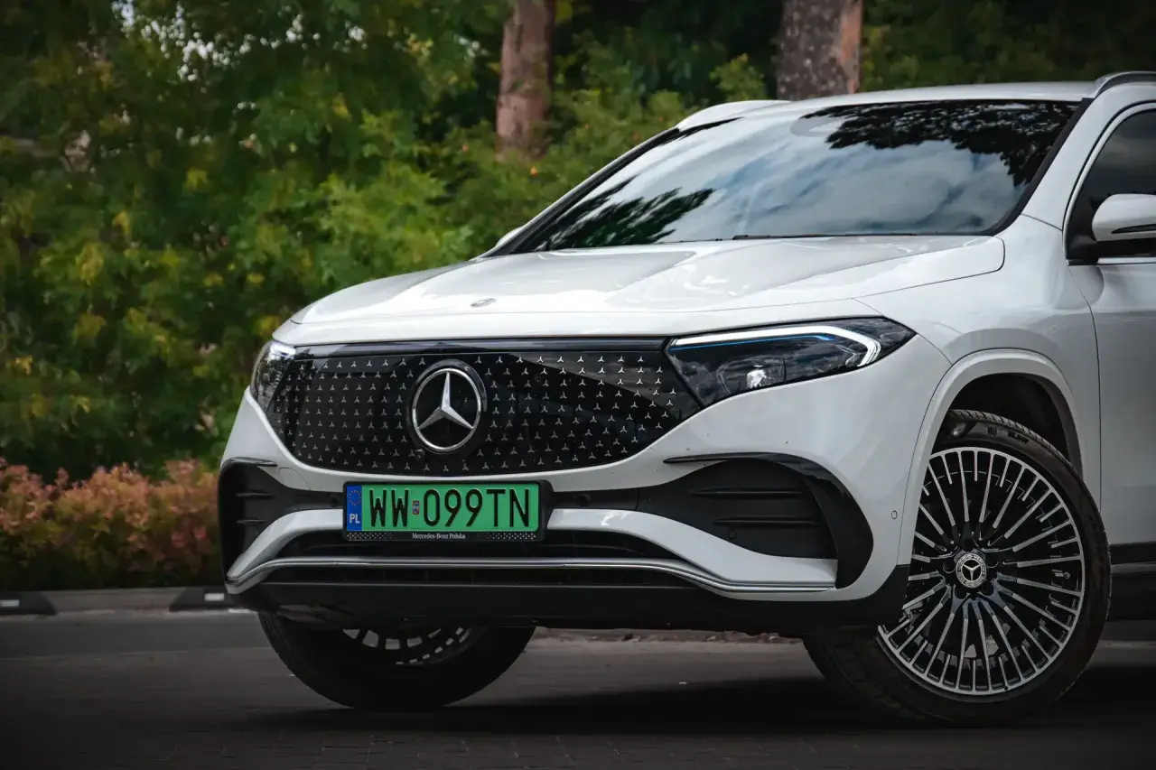 Biały Mercedes EQA z zieloną tablicą rejestracyjną WW 099TN na tle zieleni.