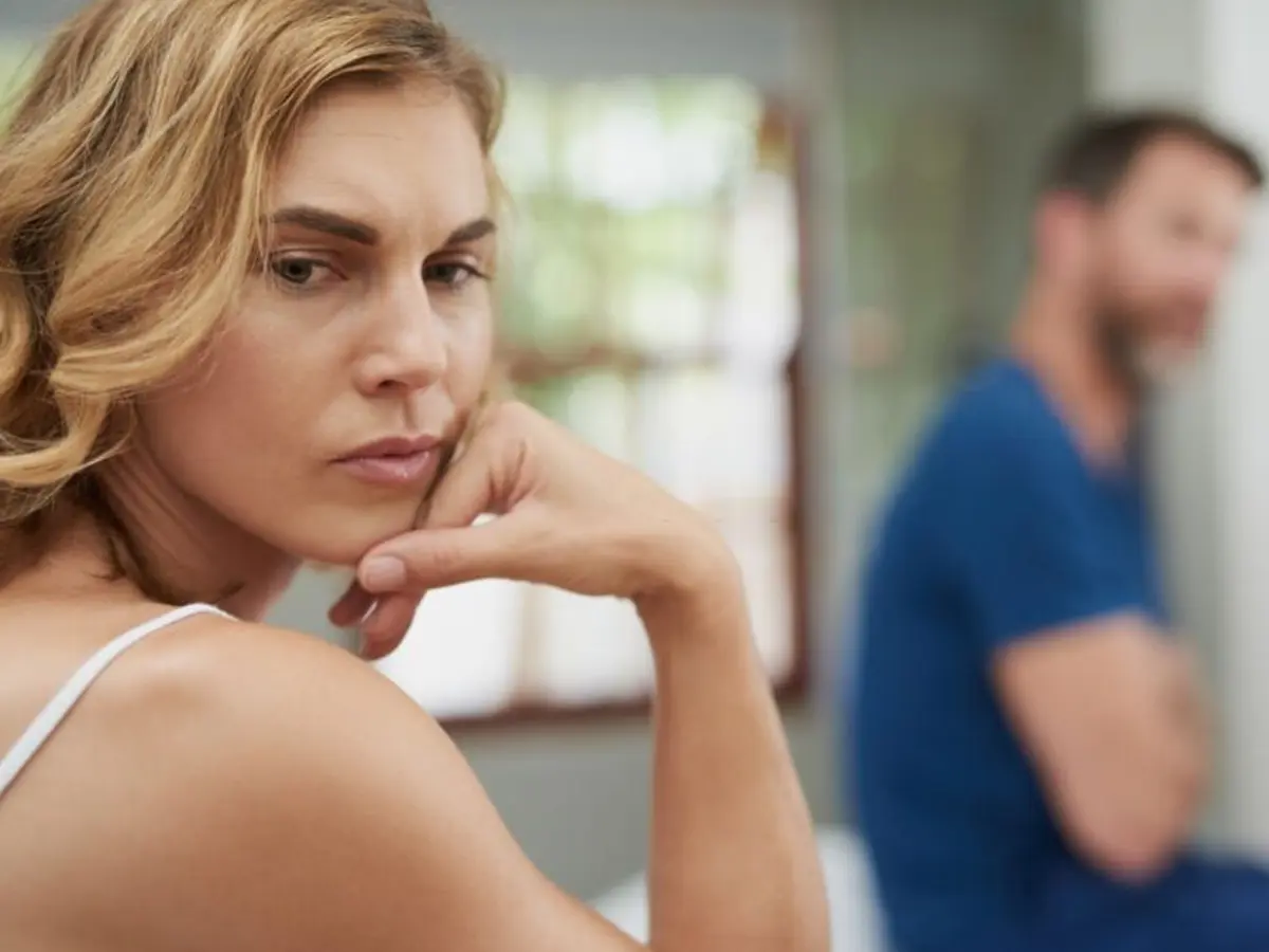A woman looks worried, with a man blurred in the background.