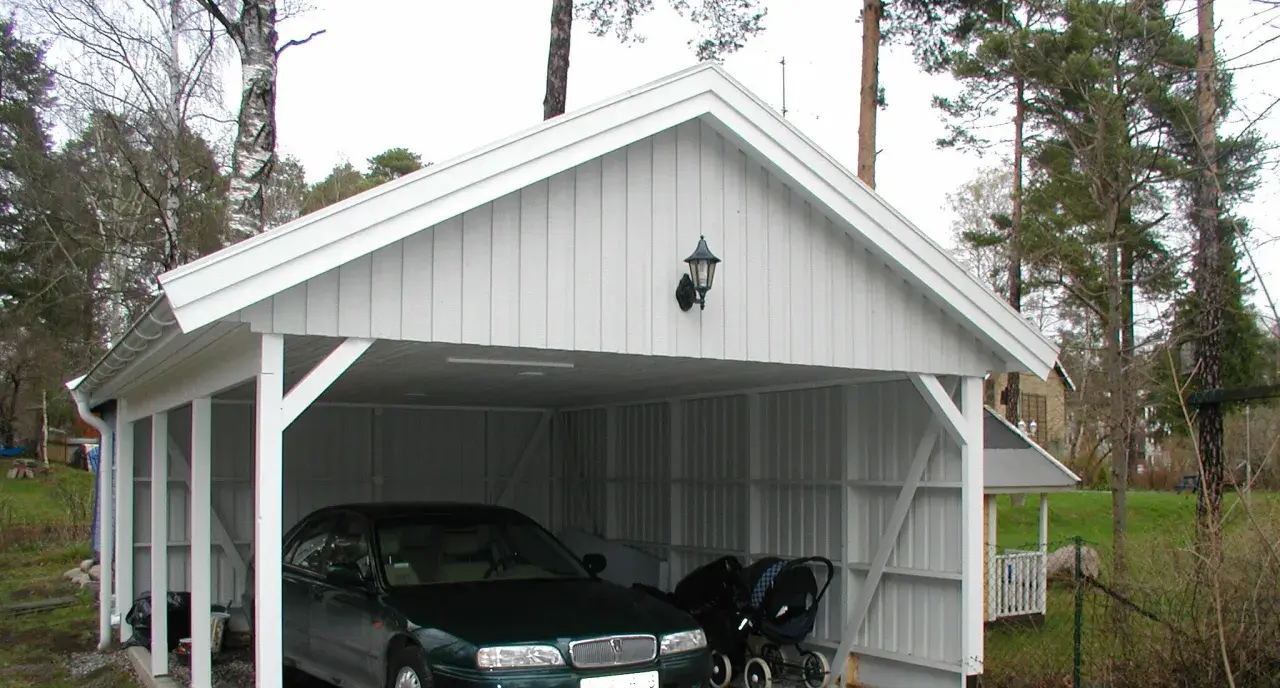 Vit carport på plintar med en bil och barnvagn.