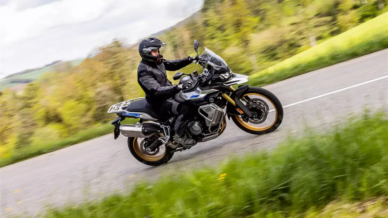 Ein Fahrer auf einer Voge DS 900 X kurvt auf einer Landstraße durch eine grüne Landschaft.