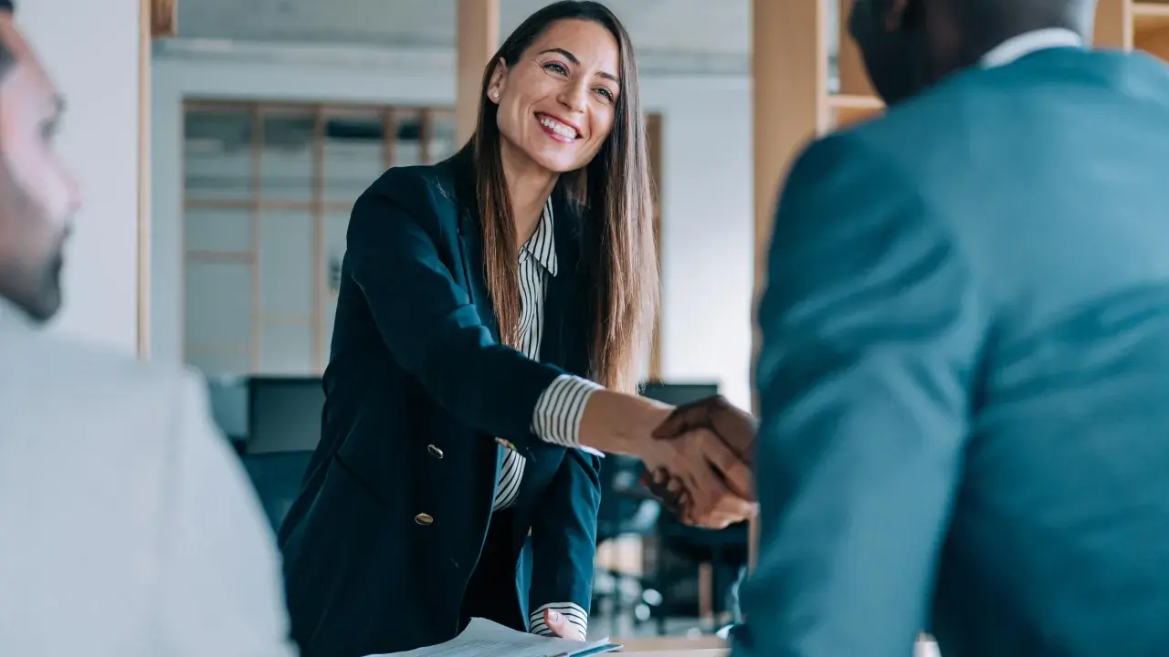 Donna sorridente stringe la mano a un collega, un momento chiave per l'employee experience.