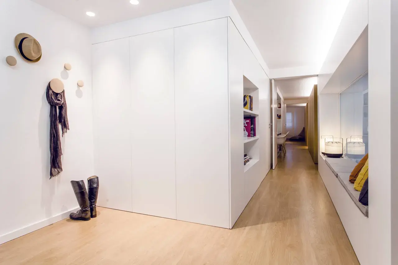 Un recibidor panelado moderno con suelo de madera, estanterías empotradas, un sombrero y bufanda colgados, y botas de montar.