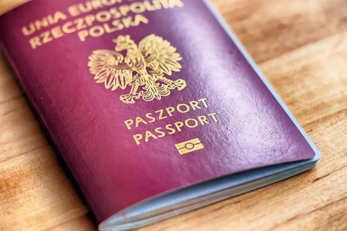 Ciemnoczerwony paszport biometryczny Rzeczypospolitej Polskiej z godłem i napisem "PASZPORT PASSPORT" na drewnianym tle.